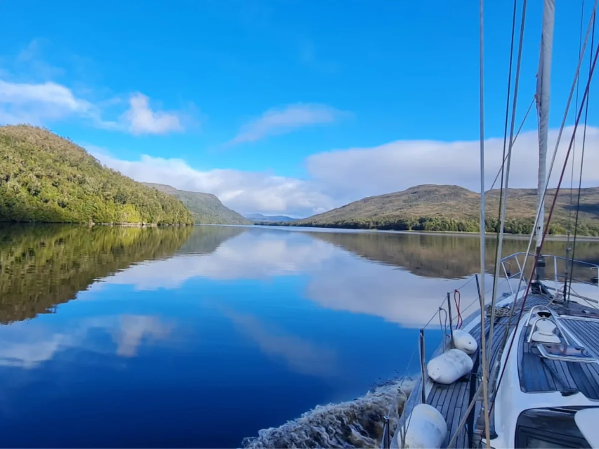 Velero navegando un canal del Archipiélago de los Chonos, aguas calmas entre cerros boscosos
